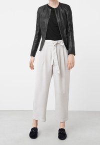 Zwarte leren jas, geribbelde zwarte top, lichtgrijze wijde broek met een strikceintuur en zwarte instappers met een decoratief accent.