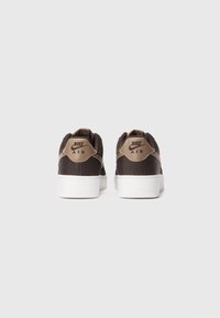 Par crnih Nike Air tenisica s teksturiranim materijalom i bež Nike logom na peti, prikazanih straga na bijeloj pozadini.