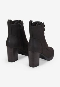 Botines negros de tacón altos, hechos de cuero liso, que cuentan con una cremallera lateral, cordones en la parte frontal y un tacón cuadrado texturizado para mayor estabilidad.