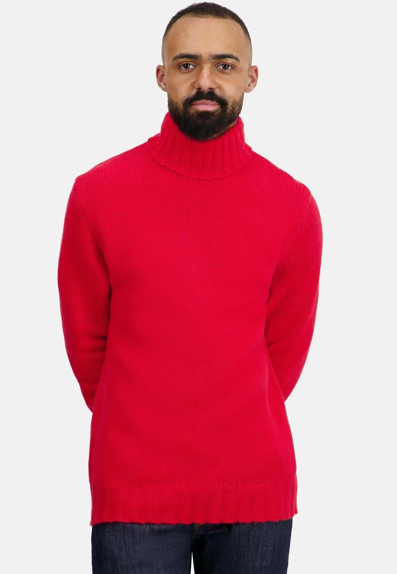 Pull à col roulé rouge en maille avec col et ourlet côtelés, présentant une coupe décontractée et une surface texturée, porté avec un jean en denim foncé.