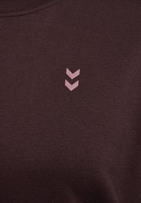 Bordeaux sweatshirt van een textuurstof. Bevat een klein roze embleem van twee naar beneden wijzende chevrons aan de linkerkant.