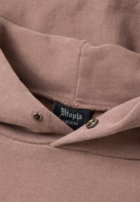 Felpa con cappuccio di colore rosa polveroso, realizzata in tessuto morbido. Presenta una texture a costine, dettagli con bottoni e un'etichetta con il marchio all'interno.