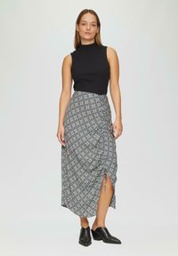 Un top noir à côtes sans manches associé à une jupe longue à motifs avec une fente latérale et un design floral en bleu, blanc et noir.
