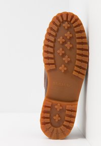 Braune Gummistiefelsohle mit tiefem Profil, versehen mit einem Muster aus Kreuzen und Rechtecken; seitlich mit "SEBAGO" markiert.