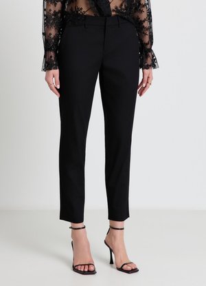 Femme portant un pantalon noir sur mesure longueur cheville, un haut en dentelle florale noire transparente et des sandales à talons noires avec des brides à la cheville.