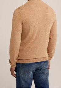 Ljusbrun stickad tröja med rund halsringning och ribbade muddar, kombinerad med blå denimjeans med bakfickor och sömnadsdetaljer.