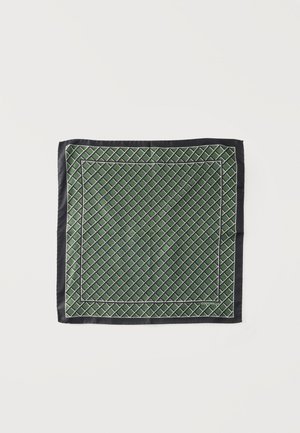 Foulard en soie verte avec motif quadrillé diagonal blanc et bordure noire, posé à plat sur fond blanc.