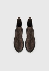 Bottes chelsea en daim marron avec une surface texturée, des panneaux latéraux élastiques et une épaisse semelle en caoutchouc noir.