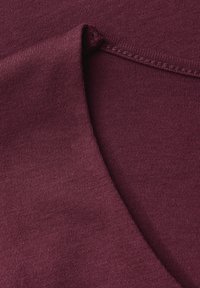 Burgundowa tkanina o gładkiej fakturze i zaokrąglonym brzegu, z delikatnym wzorem dzianiny i widocznymi detalami szwów.