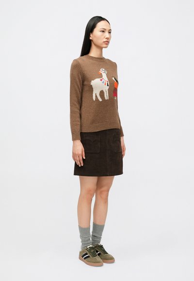 Pruun kootud kampsun, millel on põhjapõdra ja kujundite motiiv, kombineeritud tumepruuni seemismaterjalist seeliku kanssa. Hallid põlveni ulatuvad sokid ja rohelised tossud.