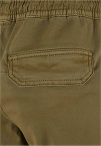 Détail de la poche arrière avec couture sur un pantalon marron à bande élastique en tissu doux.