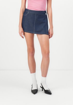 Mørkeblå denim miniskjørt med hvite sømmer og en sidelomme. Kombinert med svarte hæler og hvite ribbede sokker.