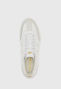 Chaussure de sport blanche avec un dessus en cuir lisse, des accents en daim gris clair, le texte "PREDATOR" en or et un système de laçage traditionnel.