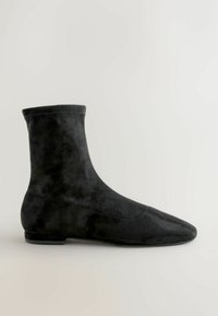 Sort ankelstøvle i glat ruskind, forlænget spids tå, strækmateriale og et minimalistisk design. Flad hæl for stabilitet.