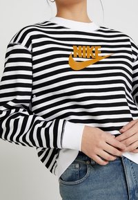 Svart och vit randig sweatshirt med rund hals. Har en orange Nike-logotyp på bröstet. Tillverkad av mjukt, strukturerat tyg.