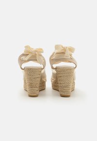 Sandalias de cuña con correas de tela beige y lazos, tacones de yute texturizado y una plantilla blanca suave. Con bordes deshilachados.