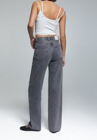 Džíny s vysokým pasem a širokými nohavicemi z texturovaného tmavě šedého denimu; obsahují zadní kapsy a štítek na pase. V kombinaci s úzkým bílým topem.