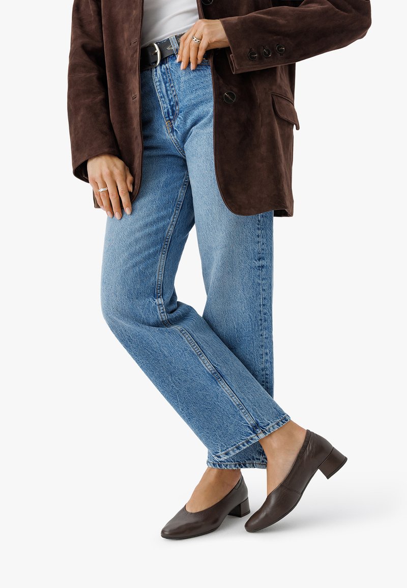 Blazer de ante marrón, top blanco, jeans rectos de mezclilla azul claro y mules oscuros de tacón con punta redonda y tacón ancho.