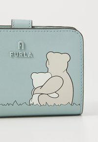 Furla skinnlommebok i lyseblå med illustrert bjørnedesign, med glatt tekstur, enkel form og logo-detalj øverst.