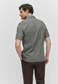 Korte mouwen, geknoopte blouse in een grijze stof met een subtiele textuur. Heeft een rechte snit en zijsplitten voor meer bewegingsvrijheid.
