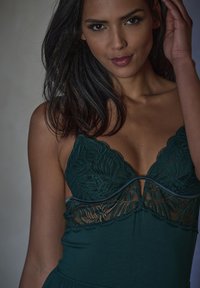 Lingerie verde scuro con dettagli in pizzo lungo il seno e tessuto morbido. Il design include una scollatura profonda e spalline morbide.