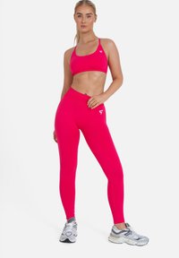 Un reggiseno sportivo rosa brillante abbinato a leggings a vita alta realizzati in tessuto elasticizzato, con un logo di marca sottile in bianco.