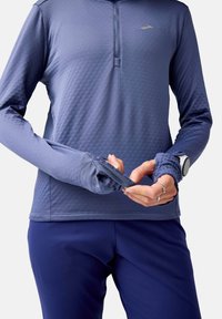 Garums piedurkņu sporta krekls ar teksturētu tumši zilu audumu, kas piedāvā pusi zips apkakli un thumbholes, apvienots ar pieguļošām tumši zila biksēm.