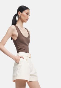 Bruine geribbelde tanktop gecombineerd met crèmekleurige high-waisted shorts met een riem. De shorts hebben zijzakken en een relaxed fit.