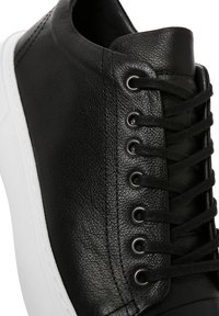 Sneaker in pelle nera con superiore testurizzato, suola in gomma bianca e sei paia di occhielli in metallo con lacci neri.