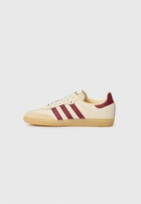 Creme sneakers med tre maroon striber, en tekstureret gummisål og blød læderoverdel. Inkluderer snørebåndslukning og polstret ankelstøtte.