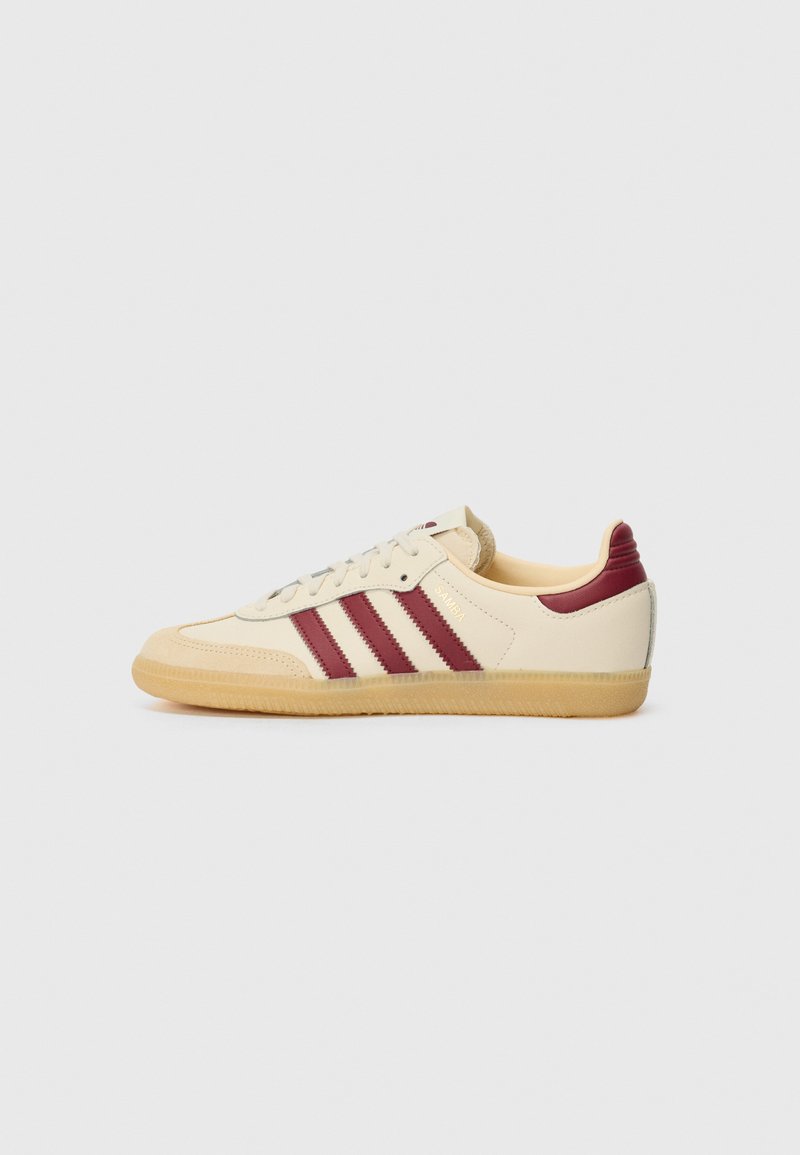Creme sneakers med tre maroon striber, en tekstureret gummisål og blød læderoverdel. Inkluderer snørebåndslukning og polstret ankelstøtte.