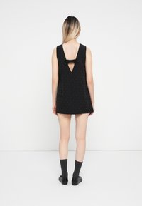 Rochie neagră fără mâneci, cu un decupaj în formă de V la spate, decorată cu o fundă. Prezintă puncte mici pentru textură, tiv drept și o croială lejeră.