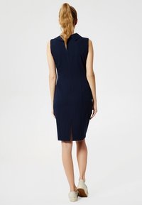 Námořnická bezramenní šaty s límcem, detailem rozparku vzadu a přiléhavým pasem. Hladká textura, délka nad kolena, minimalistický design.