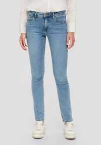 Lichtblauwe denim skinny jeans met een middelhoge taille, vijf zakken en subtiele stikdetails. Gecombineerd met witte sneakers.