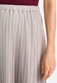 Gonna in tulle plissettato di un morbido grigio con vita elastica, caratterizzata da una texture leggera e trasparente e da un design fluido.