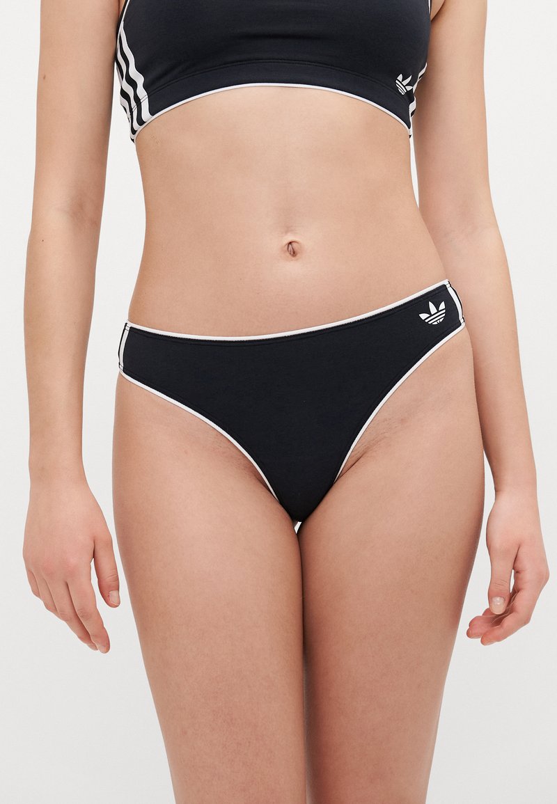 Bas de bikini noir avec des bordures blanches, présentant un design échancré et un petit logo en trois feuilles sur le côté. Matériau en coton souple et extensible.