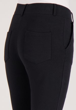 Zwarte stretchbroek met een gladde textuur, voorzien van een brede elastische tailleband en twee achterzakken. Eenvoudig, strak ontwerp zonder versieringen.