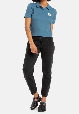 Polo bleu court avec un col et un logo brodé, associé à un jean noir droit et des sandales noires tissées.