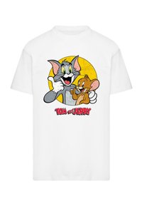Fehér pamut póló, amelyen Tom és Jerry színes grafikája látható egy sárga kör háttér előtt, az alján pedig kiemelkedő "TOM és JERRY" felirattal.