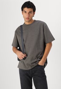Camiseta gris de manga corta en tejido texturizado, de corte relajado, con escote redondo. Se lleva con jeans de mezclilla oscura y un bolso negro de hombro.