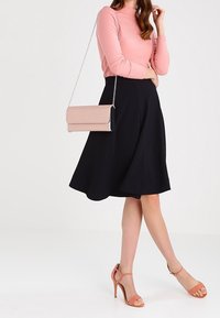 Žena v růžovém dlouhém tričku, černé sukni po kolena, růžových sandálech na vysokém podpatku a s růžovou kabelkou se stříbrným řetízkem.