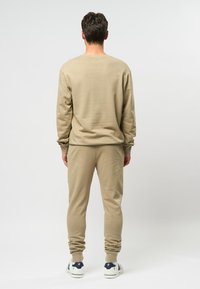 Beige sweatshirt en bijpassende joggers, gemaakt van zachte stof. Losse pasvorm met ribgebreide manchetten en tailleband. Witte sneakers maken de look af.