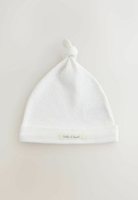 Cappellino bianco in cotone per bambino con nodo sulla sommità, delicata texture a pois e risvolto con un'etichetta piccola che riporta la scritta "little & loved".