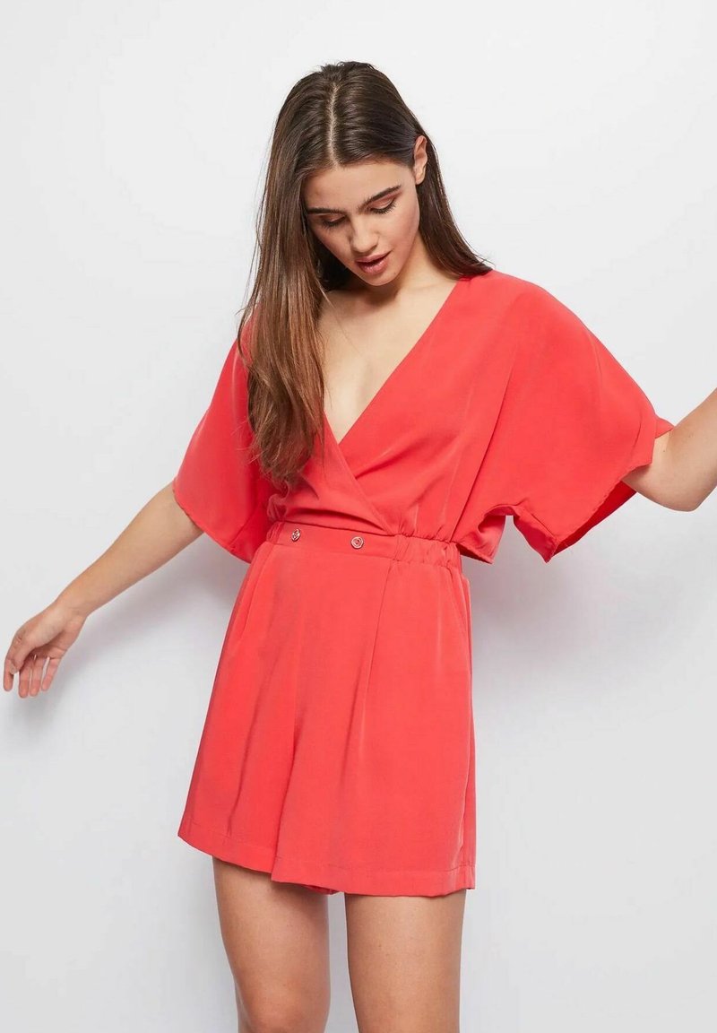 Giocattolo corallo con scollatura a V, maniche corte e larghe, e vita arricciata, con due bottoni decorativi e un tessuto leggero e morbido.