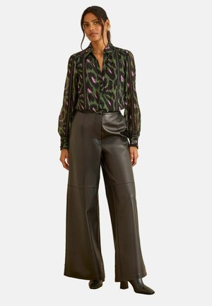 Woman wearing a green and purple patterned blouse tucked into high-waisted wide-leg black leather pants with black heeled boots.