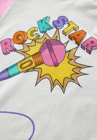 Biely textil s farebnou grafikou, na ktorej sú tučné písmená "ROCK STAR", ružový mikrofón a žlté explozívne detaily.