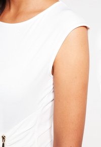 Biała sukienka bez rękawów z okrągłym dekoltem, z teksturowanymi bocznymi panelami i ozdobnym suwakiem z przodu.