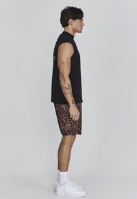 Camicetta nera senza maniche, pantaloni corti marroni con stampa leopardata, scarpe da ginnastica bianche e calzini bianchi, in mostra con texture e motivi a contrasto.