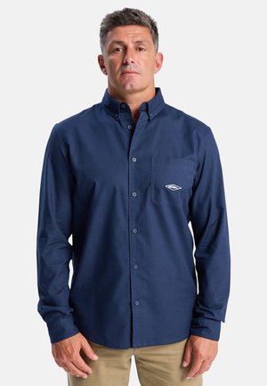 Navy blue long-sleeve button-up shirt in cotton fabric with a stitched chest pocket and logo detail, featuring a classic collar and button closure.