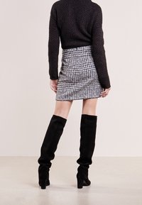 Un pull noir en tricot associé à une jupe mini en pied-de-coq noir et blanc texturée et des bottes noires en suède montant jusqu'à la cuisse avec des talons blocs.